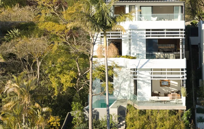 White stacked balconies with horizontal railings emerging from hillside vegetation in afternoon sun