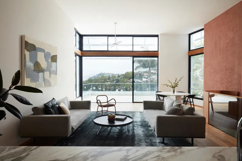 Living room overlooking water with black-framed glazing and rammed earth wall dividing adjacent spaces