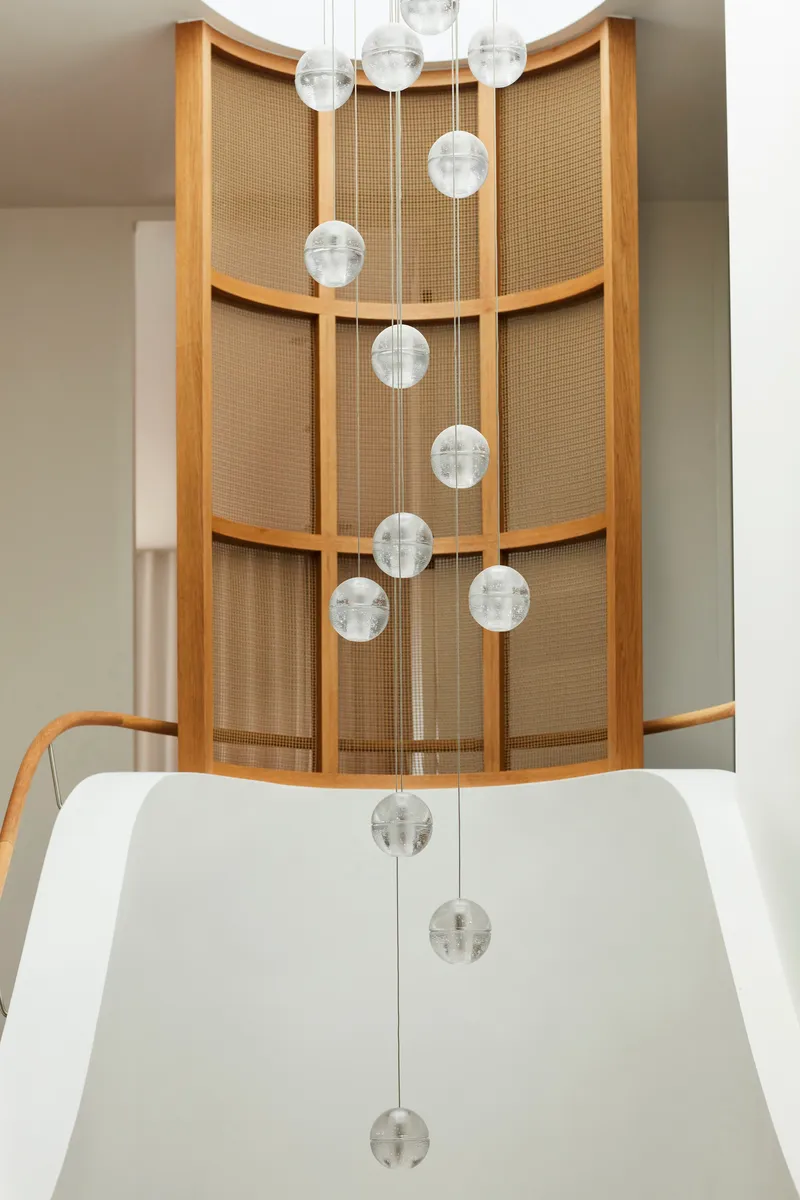 Cascading glass pendant lights in the curved stairwell with oak-framed woven cane screens