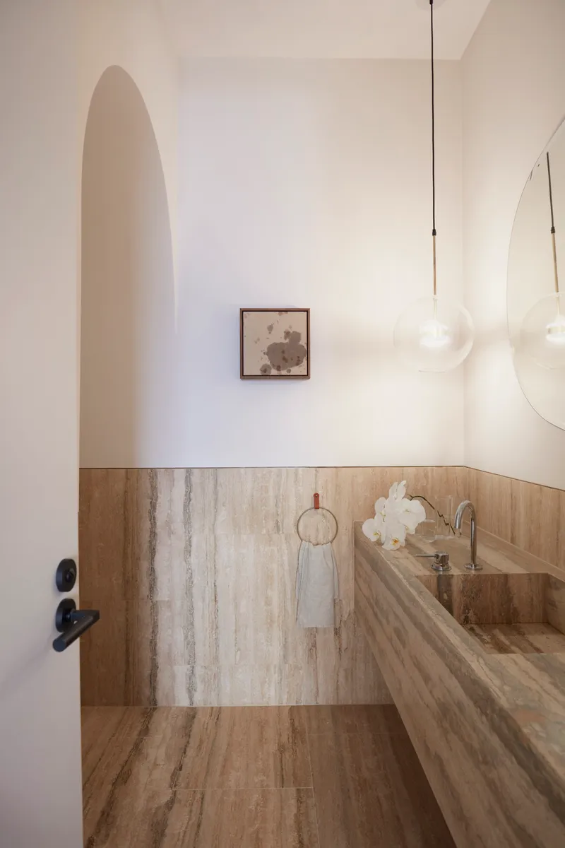 Powder room with travertine wainscoting and an arched doorway with pendant light above