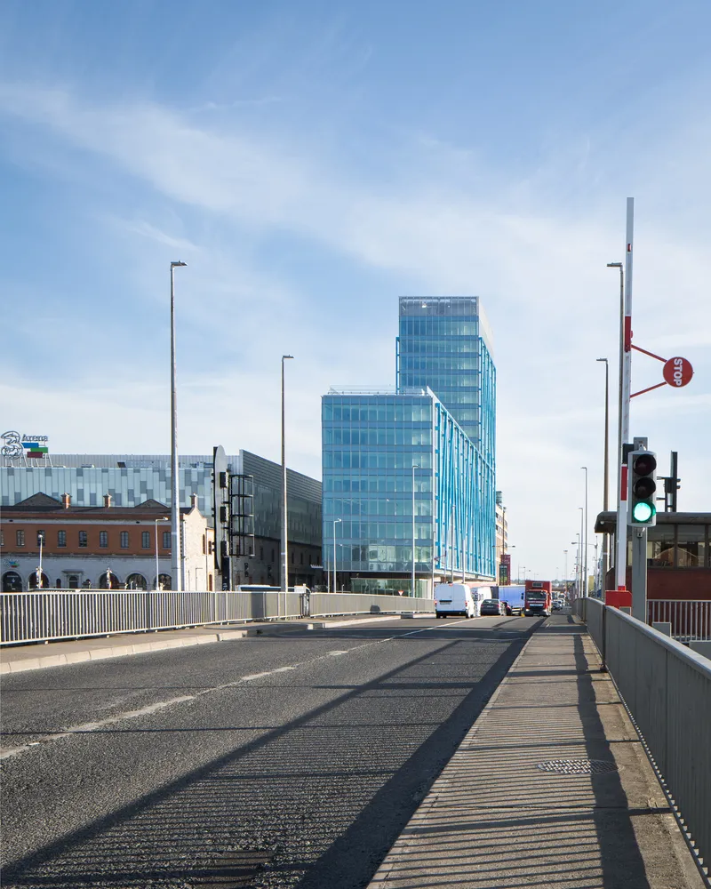 Stepped glass tower viewed from a bridge with street lights and traffic signals in morning light