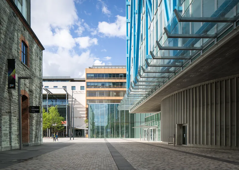 Pedestrian passage between historic masonry building and ribbed metal canopy base of glazed tower