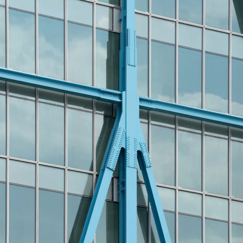 Close-up of painted blue steel bracing members crossing the curtain wall facade
