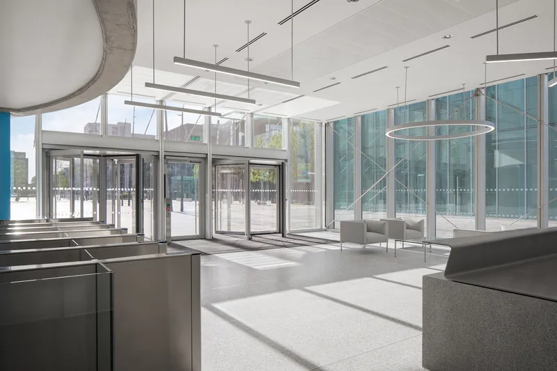 Ground floor lobby with glass revolving doors and pendant light fixtures filtering daylight onto terrazzo flooring