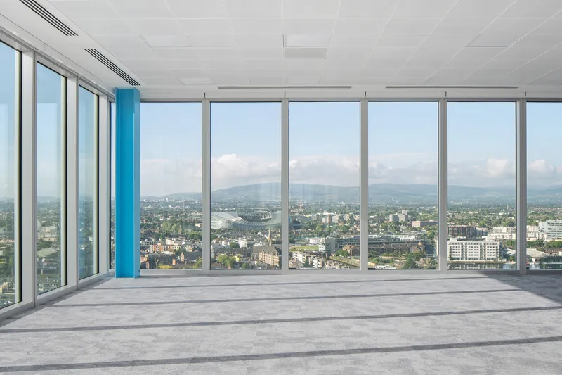 Floor-to-ceiling glazing with blue mullion accents overlooking the cityscape under a cloudy sky