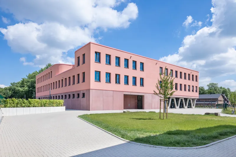 Side view of the pink rendered volumes with punctured windows beside a paved path