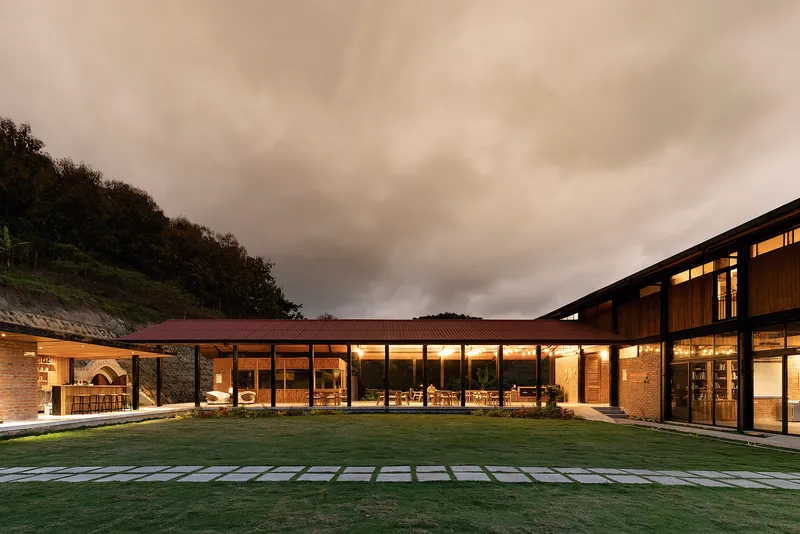 Courtyard view of the L-shaped glazed facade linking brick and timber volumes at dusk