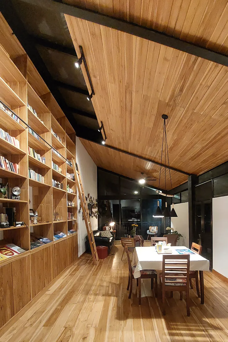 Dining area with timber bookshelf wall and slat ceiling under exposed black steel beams