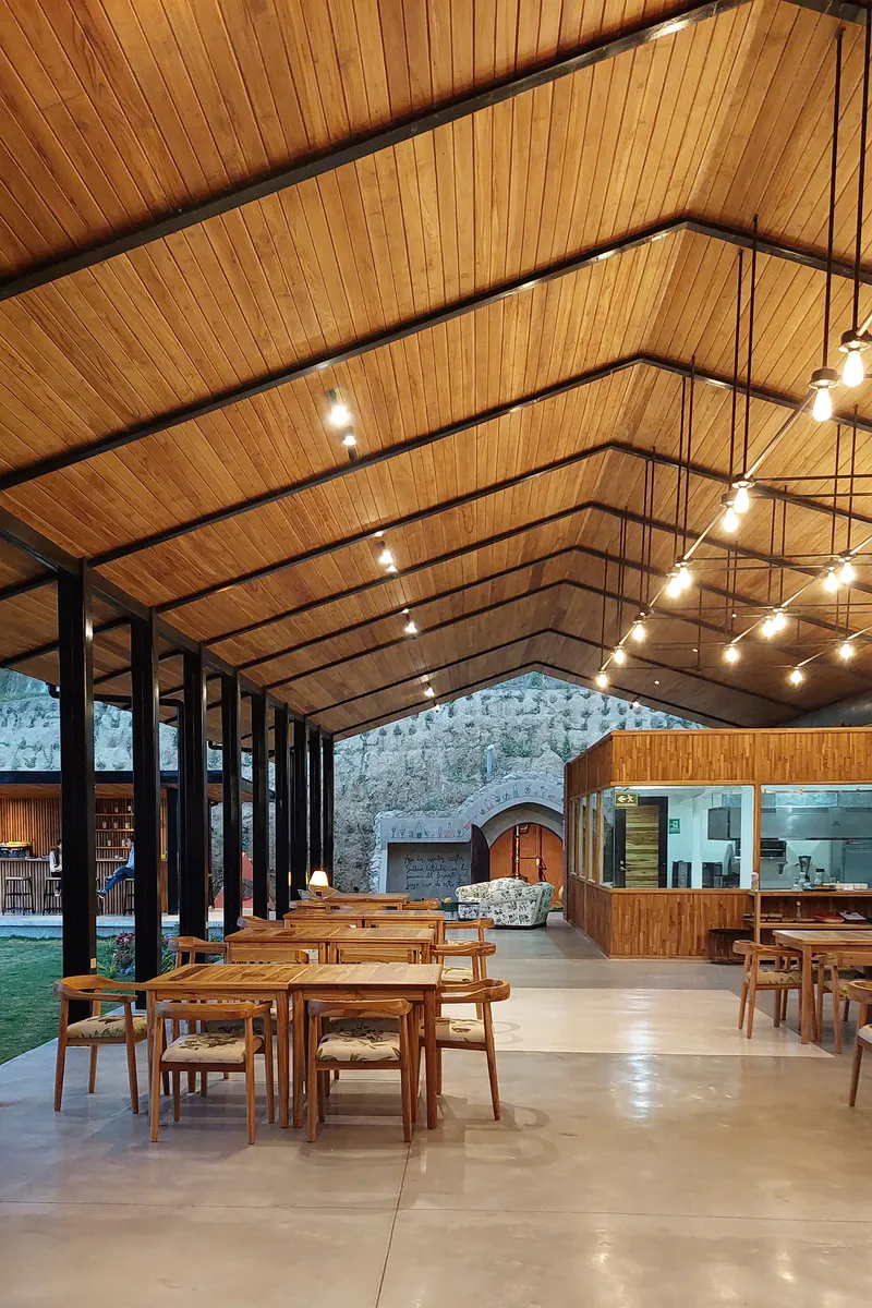 Dining hall with gabled timber ceiling, steel columns and string lights above timber tables
