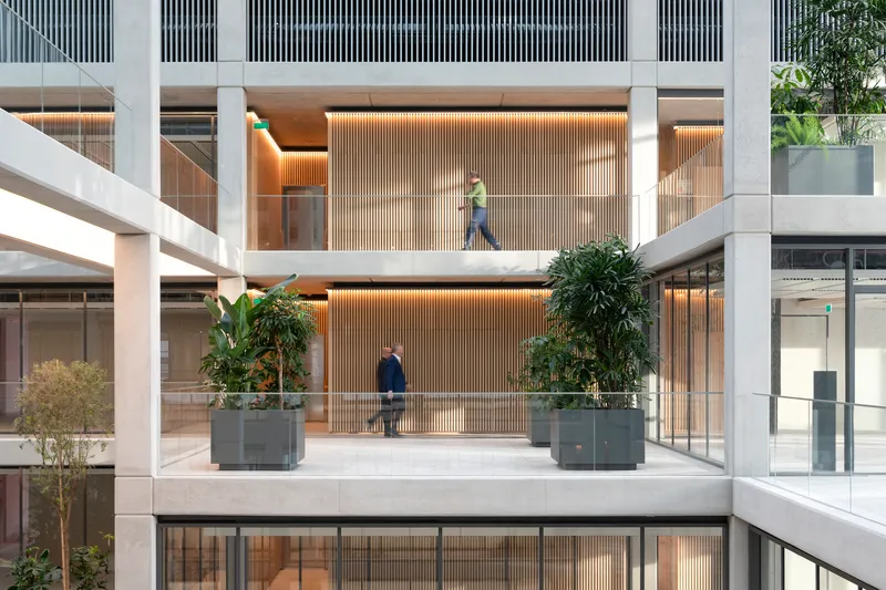 Interior atrium with concrete bridges connecting levels lined with vertical timber slats and planted containers