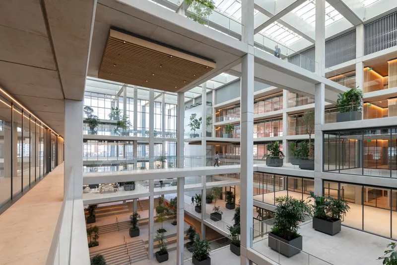Atrium corridor view showing suspended timber ceiling panels and potted trees on multiple levels