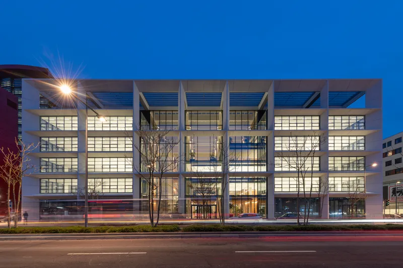 Front facade at twilight with illuminated glazing framed by deep concrete beams and bare trees