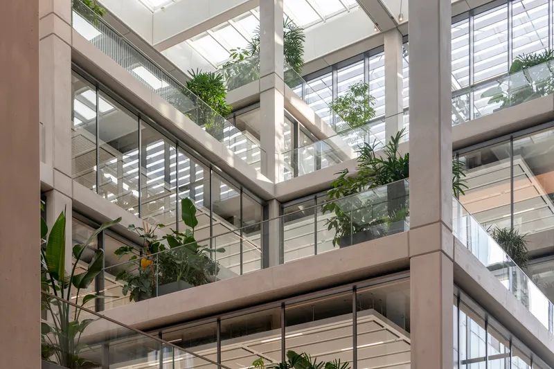 Atrium view with stacked balconies, glass railings, and potted plants beneath a glazed skylight