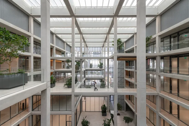 Central courtyard flanked by concrete columns and horizontal balconies with people crossing below
