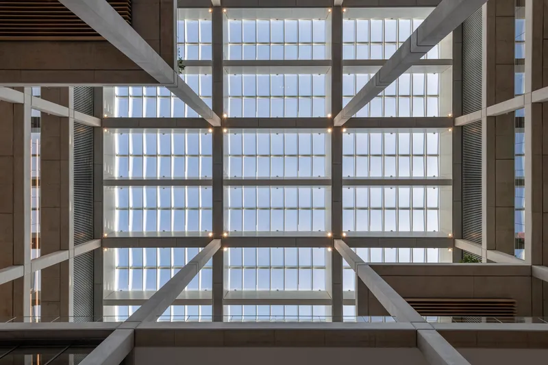 Upward view through concrete beams to a gridded glass ceiling diffusing daylight