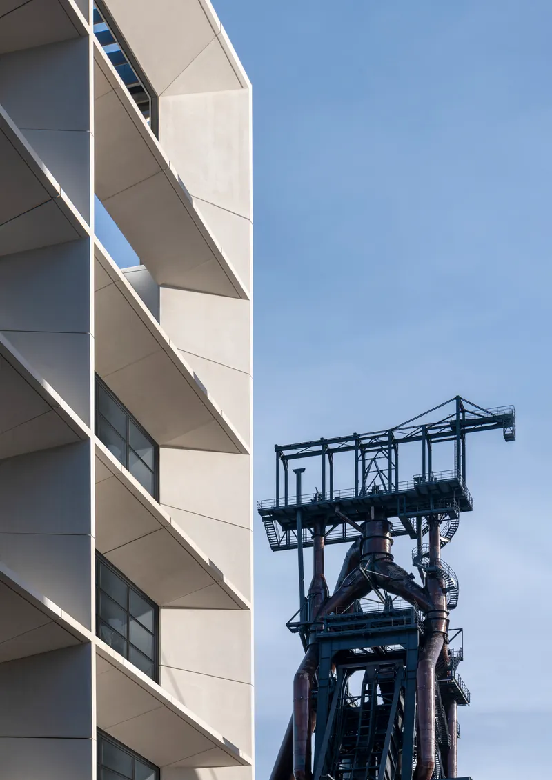 Facade detail with recessed balconies beside a black steel mining headframe structure
