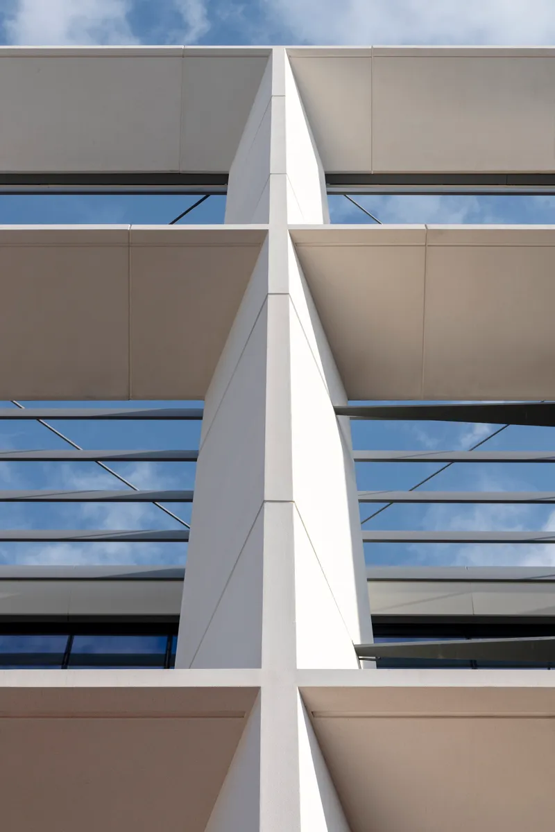 White triangular column dividing horizontal bands of operable windows and beige panel cladding under blue sky
