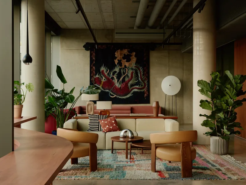 Lounge area with curved seating, exposed ceiling ducts, and a textile dragon tapestry hung on the rear wall