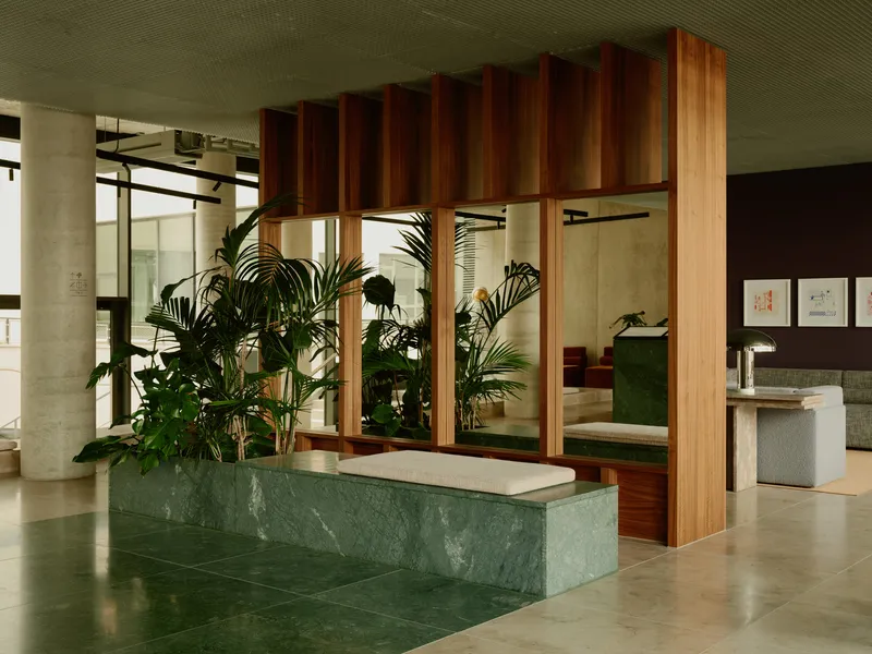 Green marble reception counter beneath a suspended timber slat installation with indoor palms
