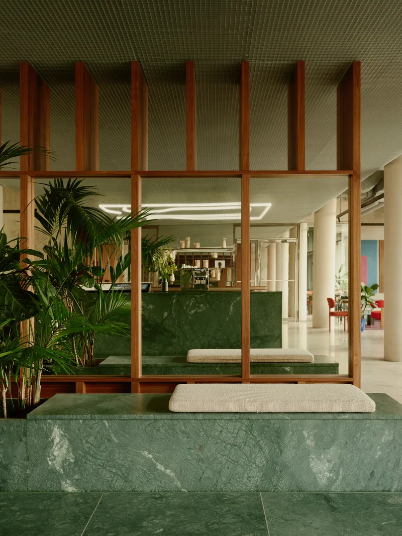Green marble bench with cushion seating below a timber screen partition and planted palms