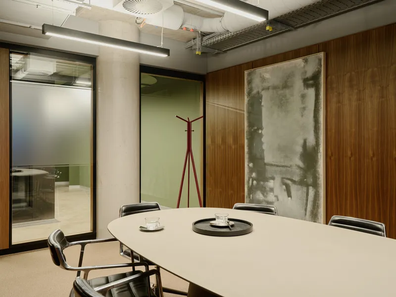 Meeting room with oval table and exposed concrete ceiling ducts beside wood paneling and artwork