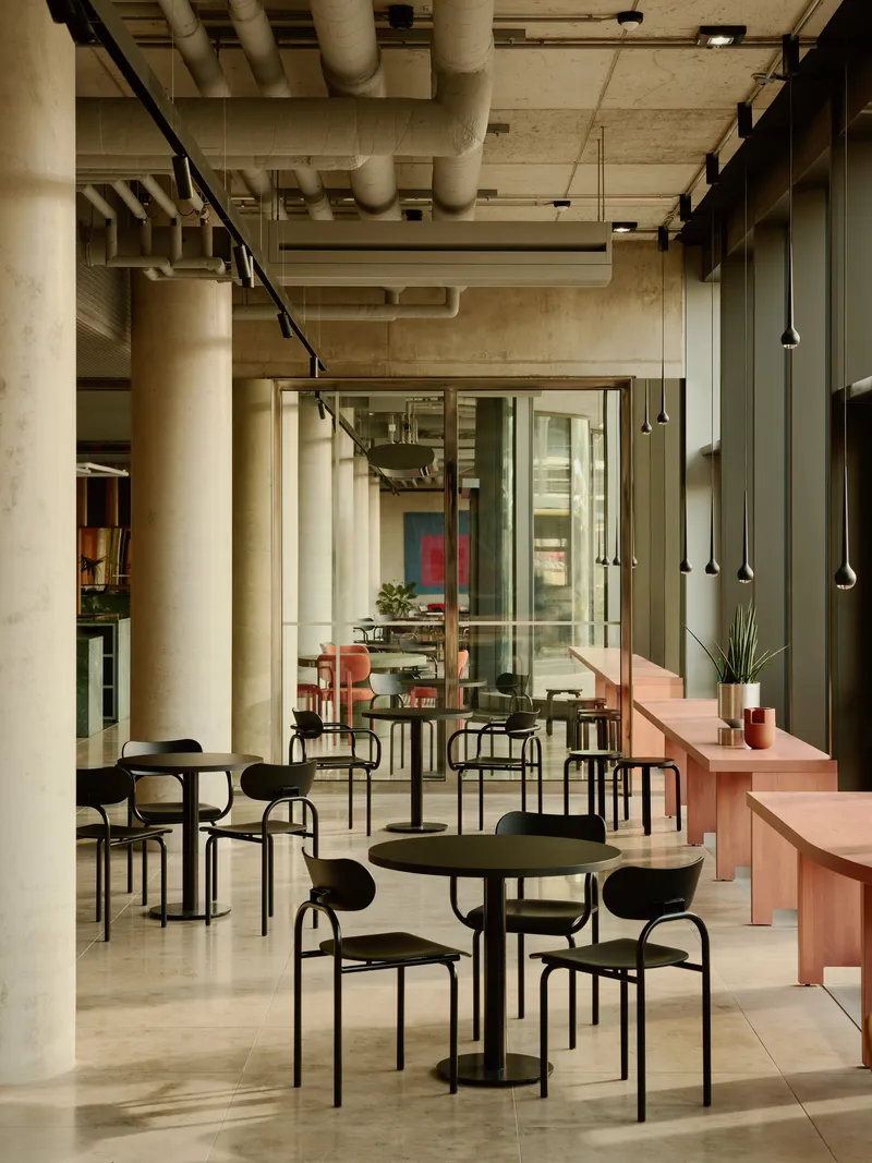 Cafe area with round tables and pendant lights along cylindrical concrete columns and exposed structure