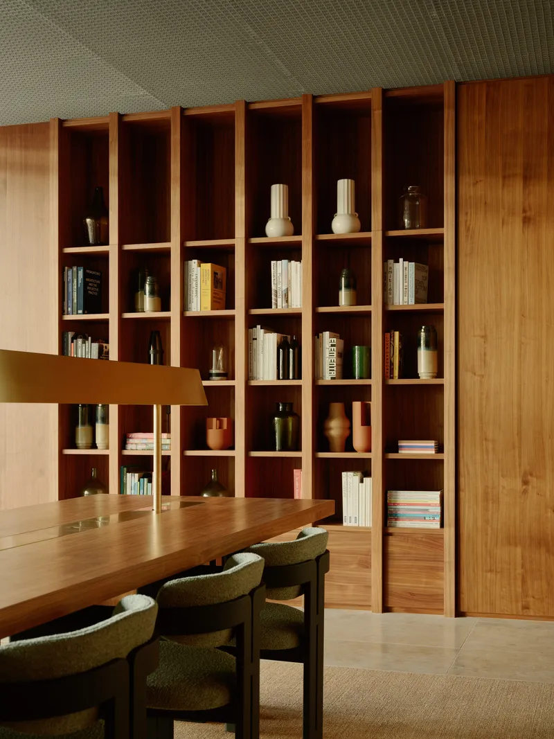 Timber shelving wall with ceramic objects and books beside dining table with green upholstered chairs
