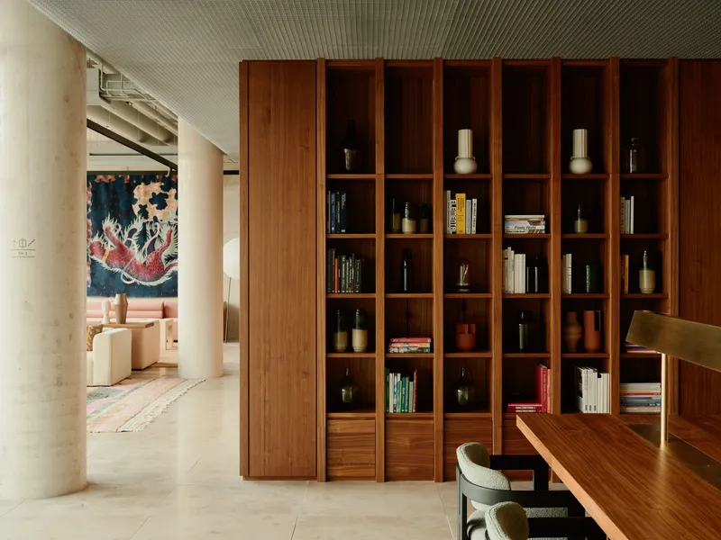 Floor-to-ceiling wooden bookcase dividing dining area from living room with artwork visible beyond cylindrical columns