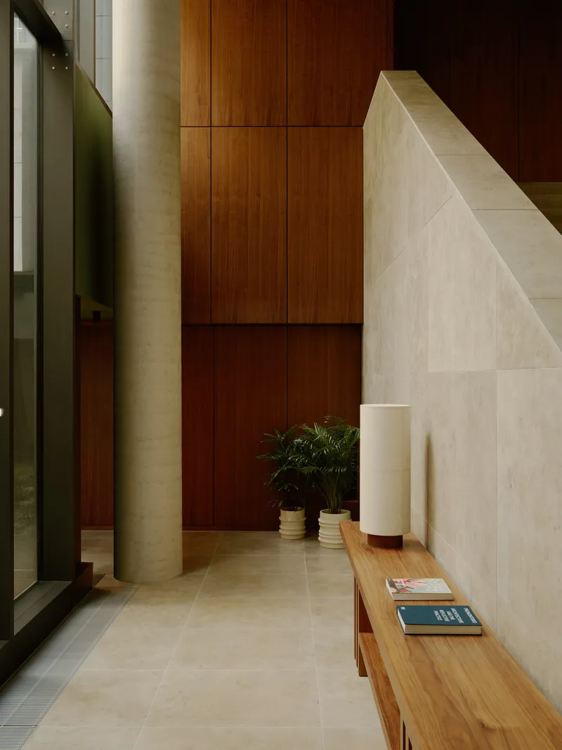 Entry corridor with cylindrical column, limestone stair volume, and timber bench with potted plant