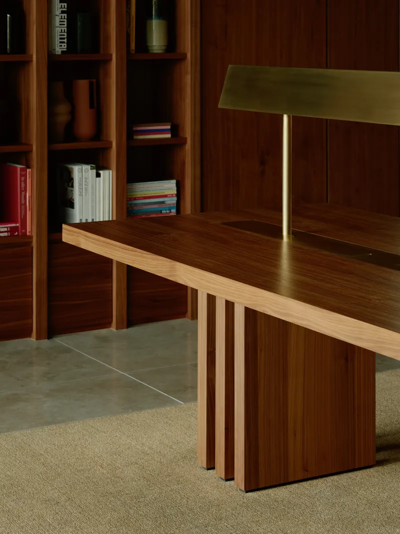 Close-up of timber table with brass lamp and slatted base beside walnut shelving unit