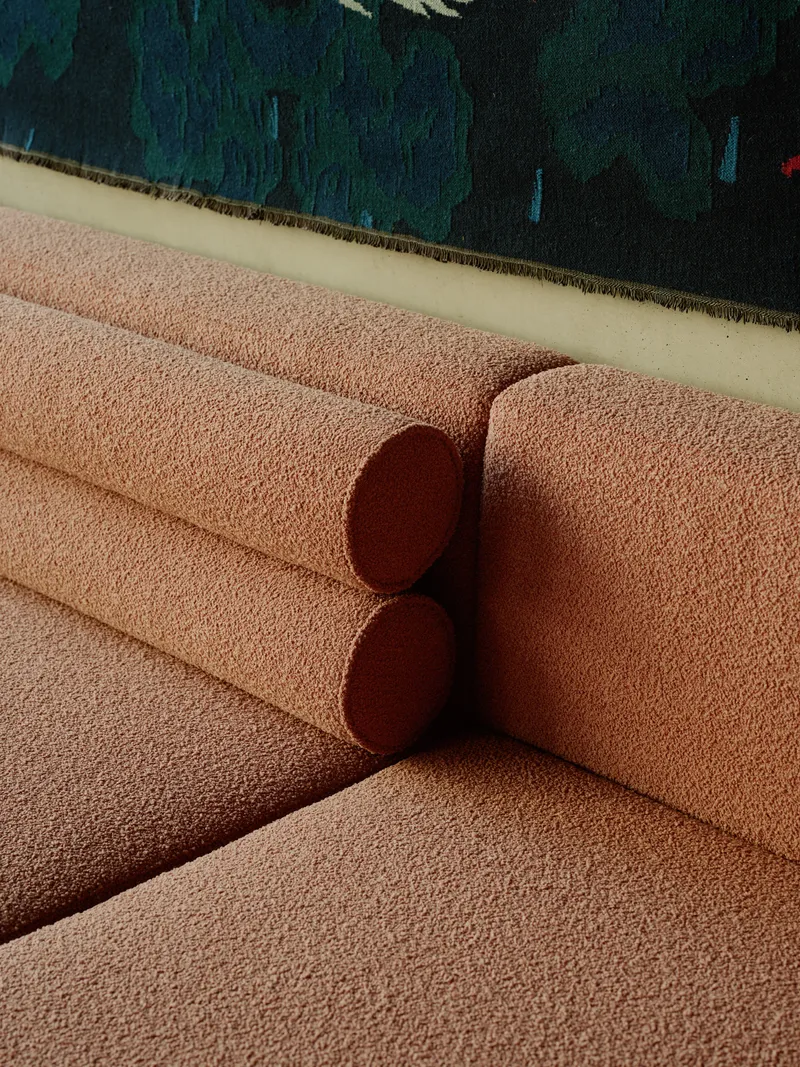 Close-up of a pink textured sofa with cylindrical cushion against a deep blue tapestry