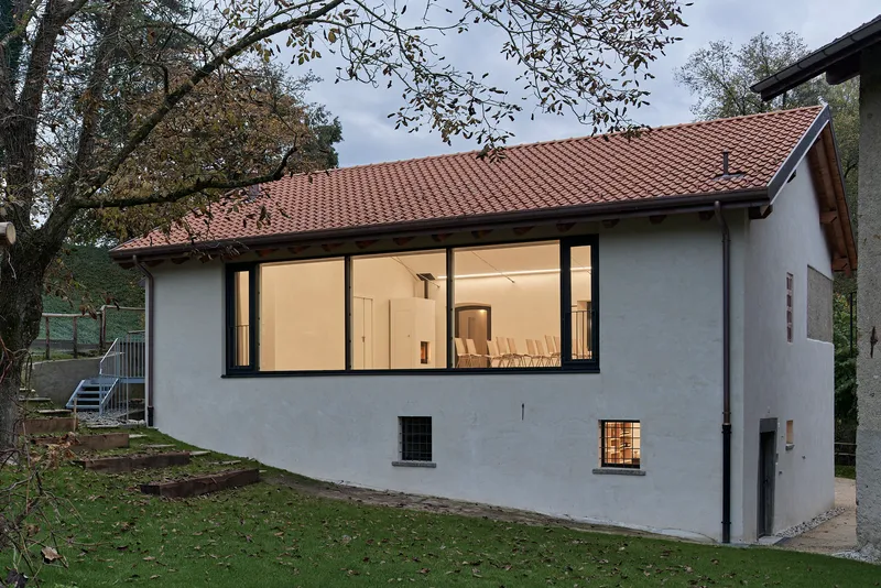 Garden view of the white rendered facade with large picture window and red clay tile roof under overhanging branches