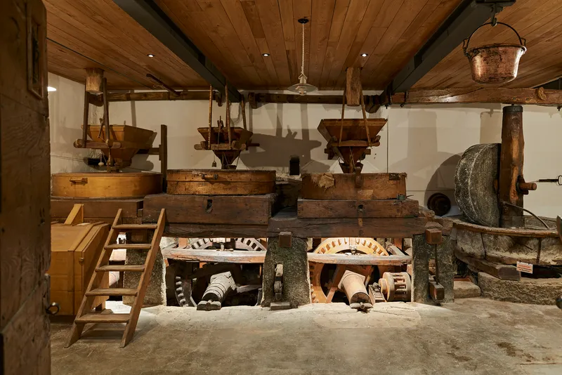 Historic mill machinery with wooden hoppers, stone wheels and timber beams under a plank ceiling