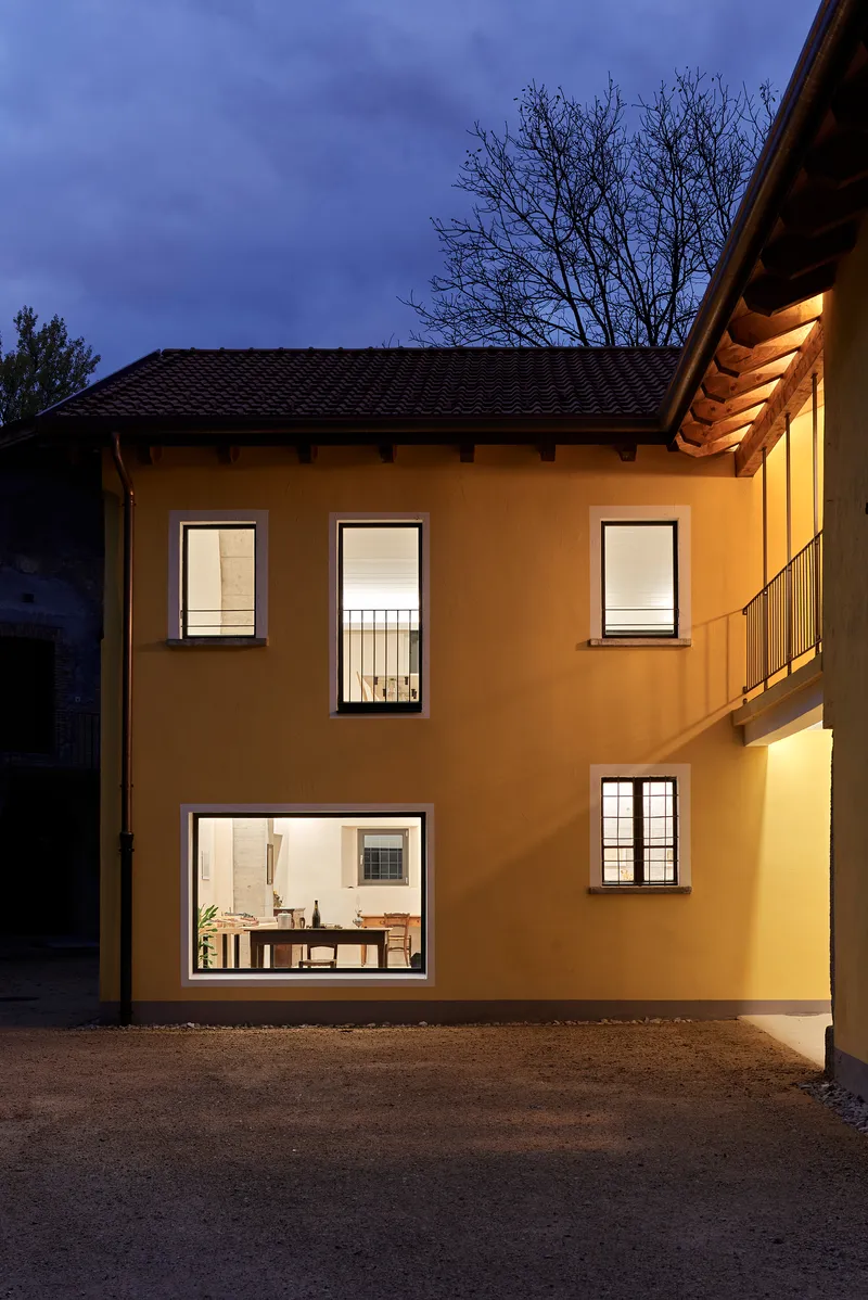 Ochre stucco facade with illuminated windows and exposed timber eaves at dusk