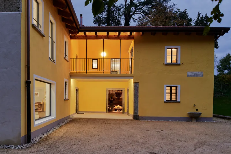 Courtyard view showing ochre volumes with illuminated openings and gravel surface at twilight