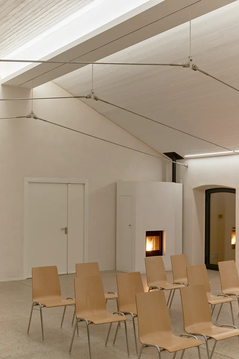 Vaulted ceiling with tensioned fabric panels and cable supports above rows of plywood chairs and fireplace insert