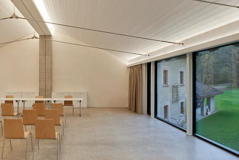 Meeting room with floor-to-ceiling glazing framing view of hillside and weathered stone building beyond