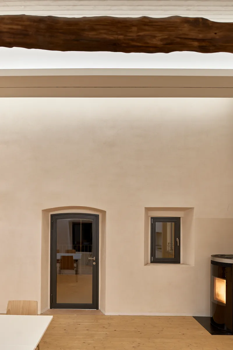 Interior wall with arched doorway, square window opening, exposed timber beam overhead, and pellet stove
