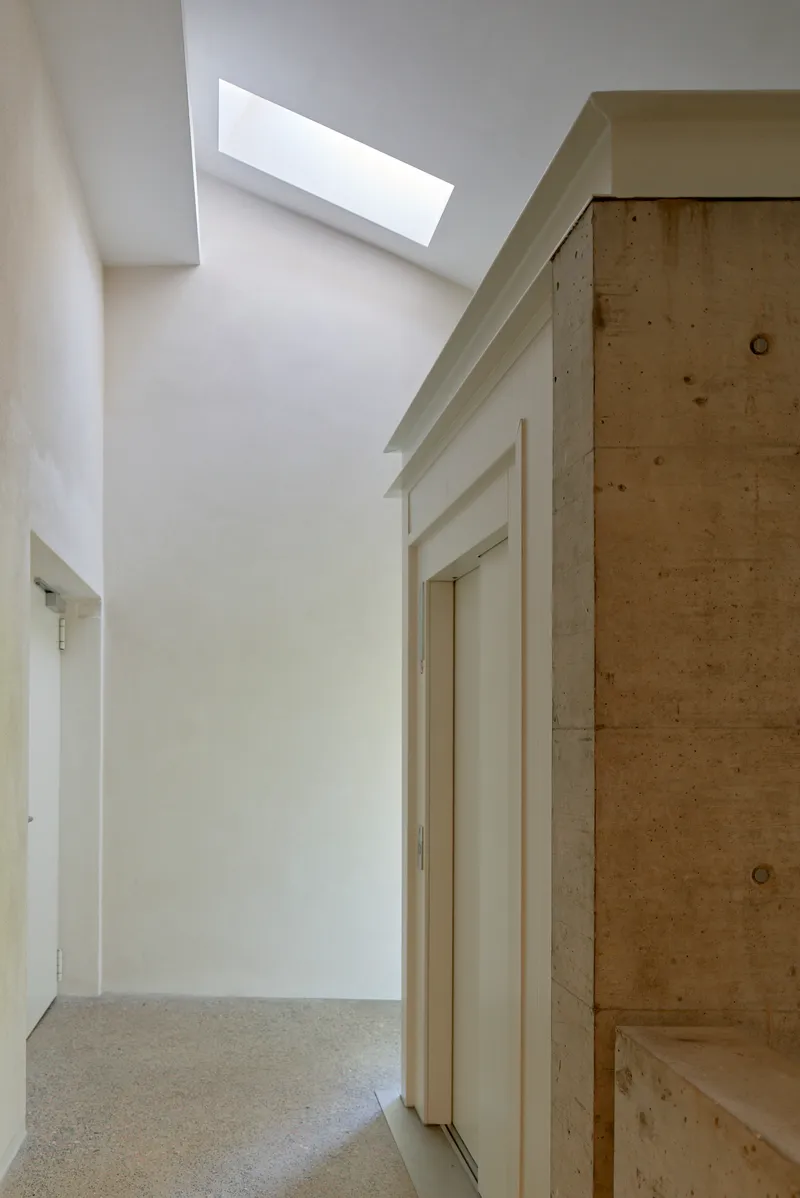 Interior hallway with plywood built-in storage and rectangular skylight casting daylight on white walls