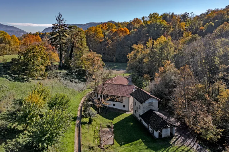 Aerial view of white gabled building complex nestled in rolling hills with autumn foliage