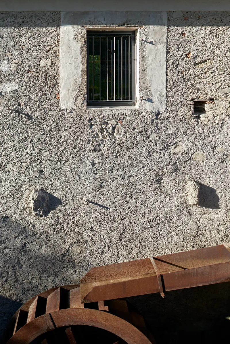 Barred window in weathered stucco facade with rusted ironwork casting afternoon shadows