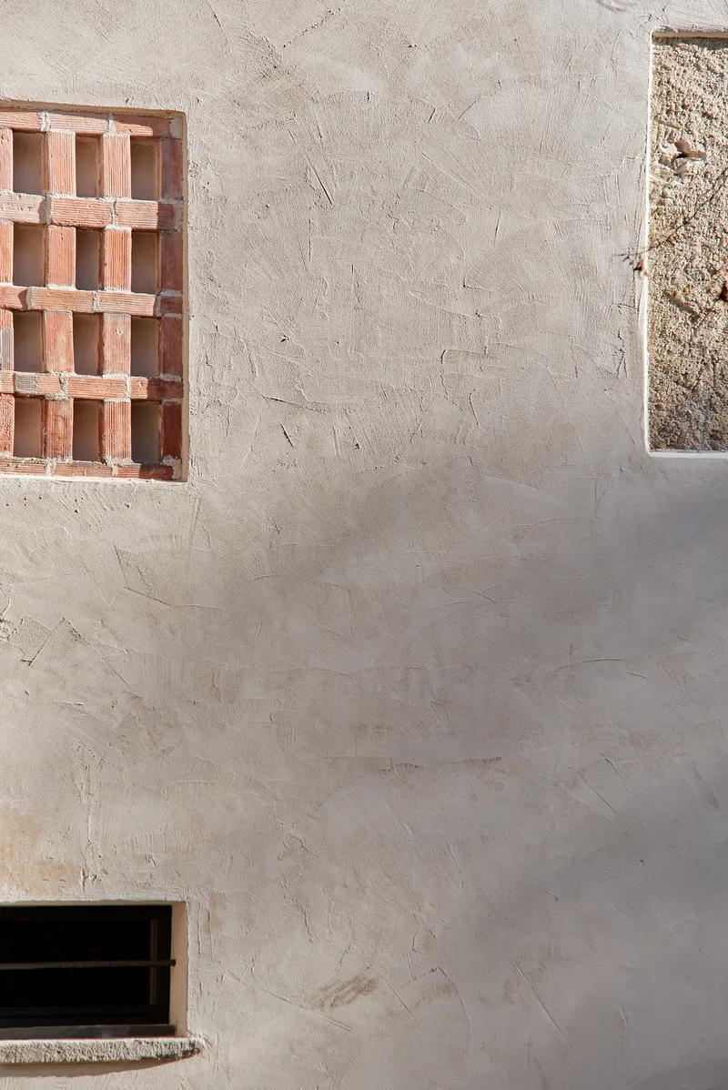 Textured plaster wall with terracotta brick screen window and narrow concrete slit opening