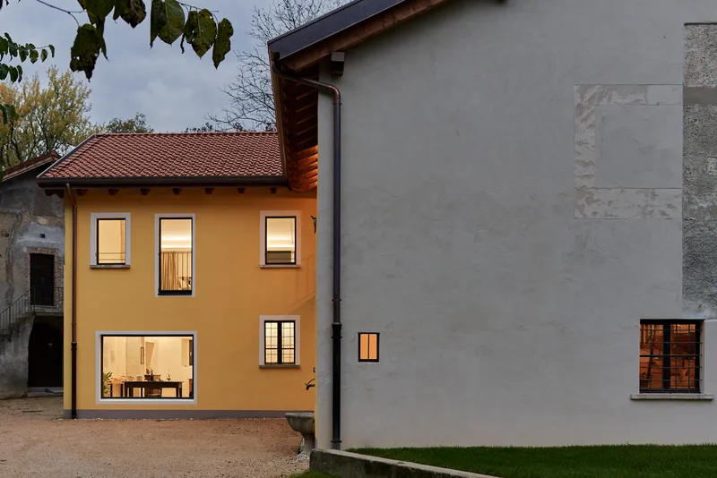 Courtyard view of illuminated yellow house and grey rendered addition at dusk