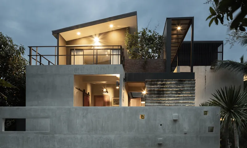 Concrete retaining walls and illuminated interior spaces at dusk with planted beds and palm fronds