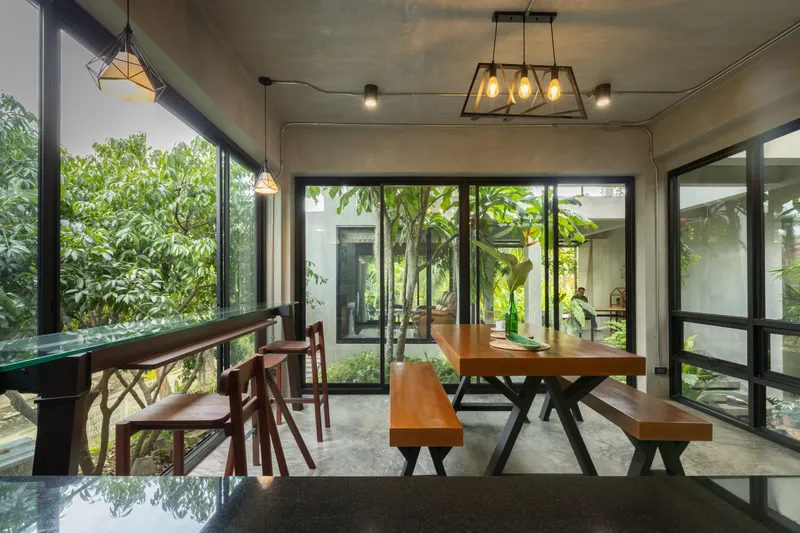 Dining area with timber furniture and concrete ceiling overlooking the interior planted courtyard through floor-to-ceiling glazing