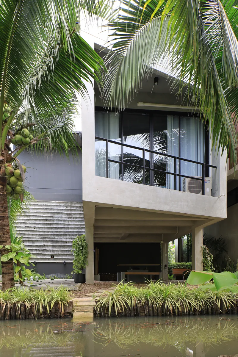 Cantilevered balcony with metal railing framed by coconut palms above a still water canal