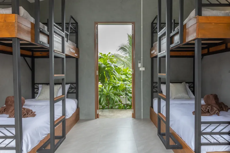 Dormitory room with timber and steel bunk beds flanking a doorway to a planted courtyard