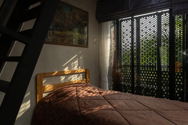 Bedroom with perforated black screens filtering morning sunlight onto a timber bed frame