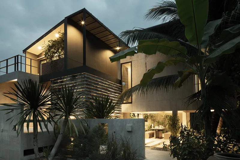 Concrete and timber facade with gabled roof and horizontal slat screening framed by palms at twilight