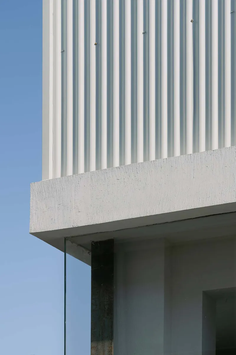 Detail of corrugated cladding meeting a cast concrete edge above a recessed glass opening